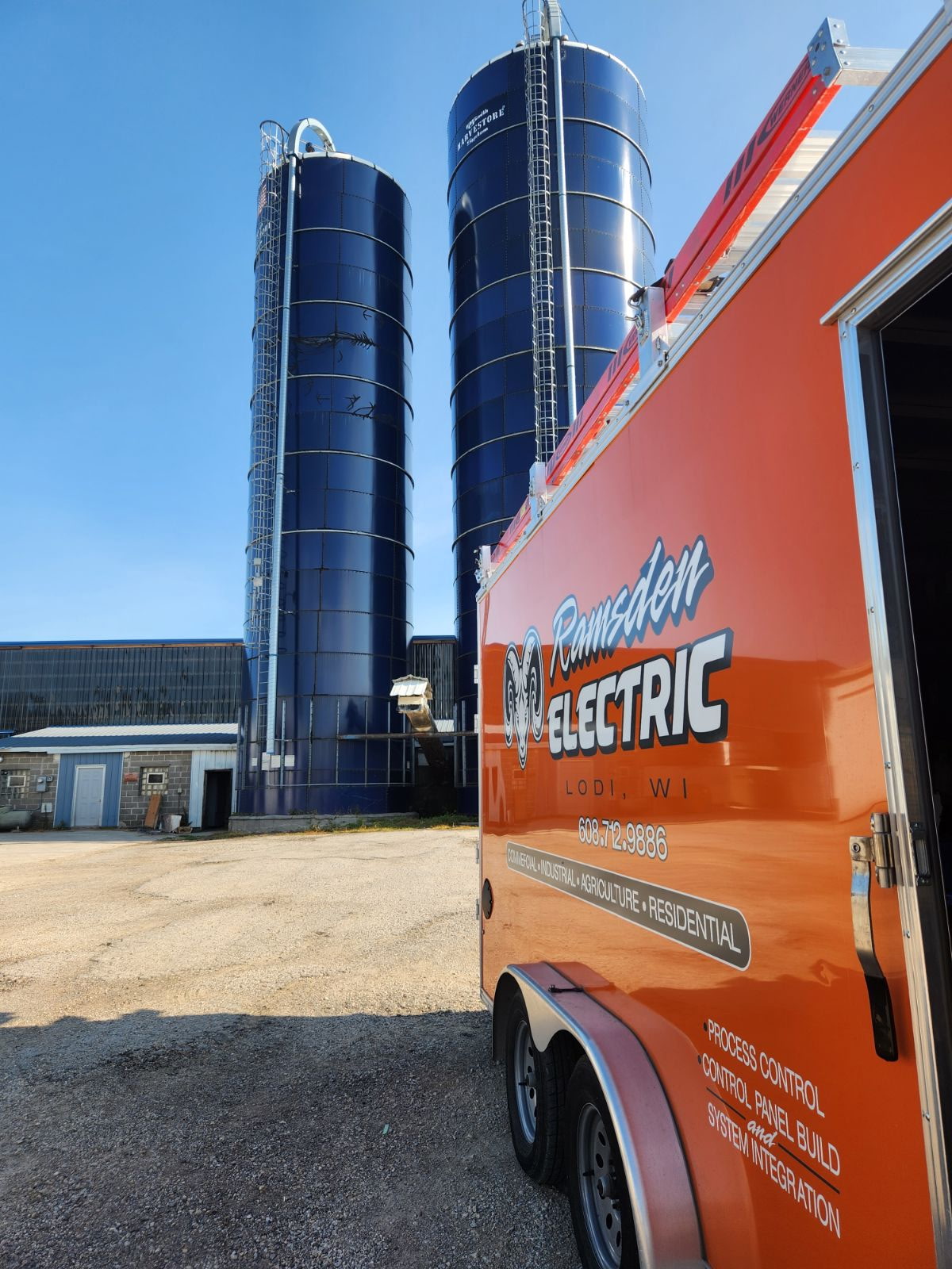 Ramsden Electric trailer parked in front of blue silos at a farm